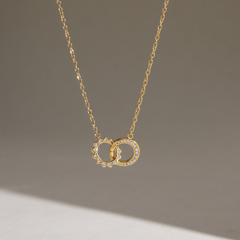 Gold tone interlocking circle necklace hanging against a pale background
