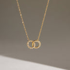 Gold tone interlocking circle necklace hanging against a pale background