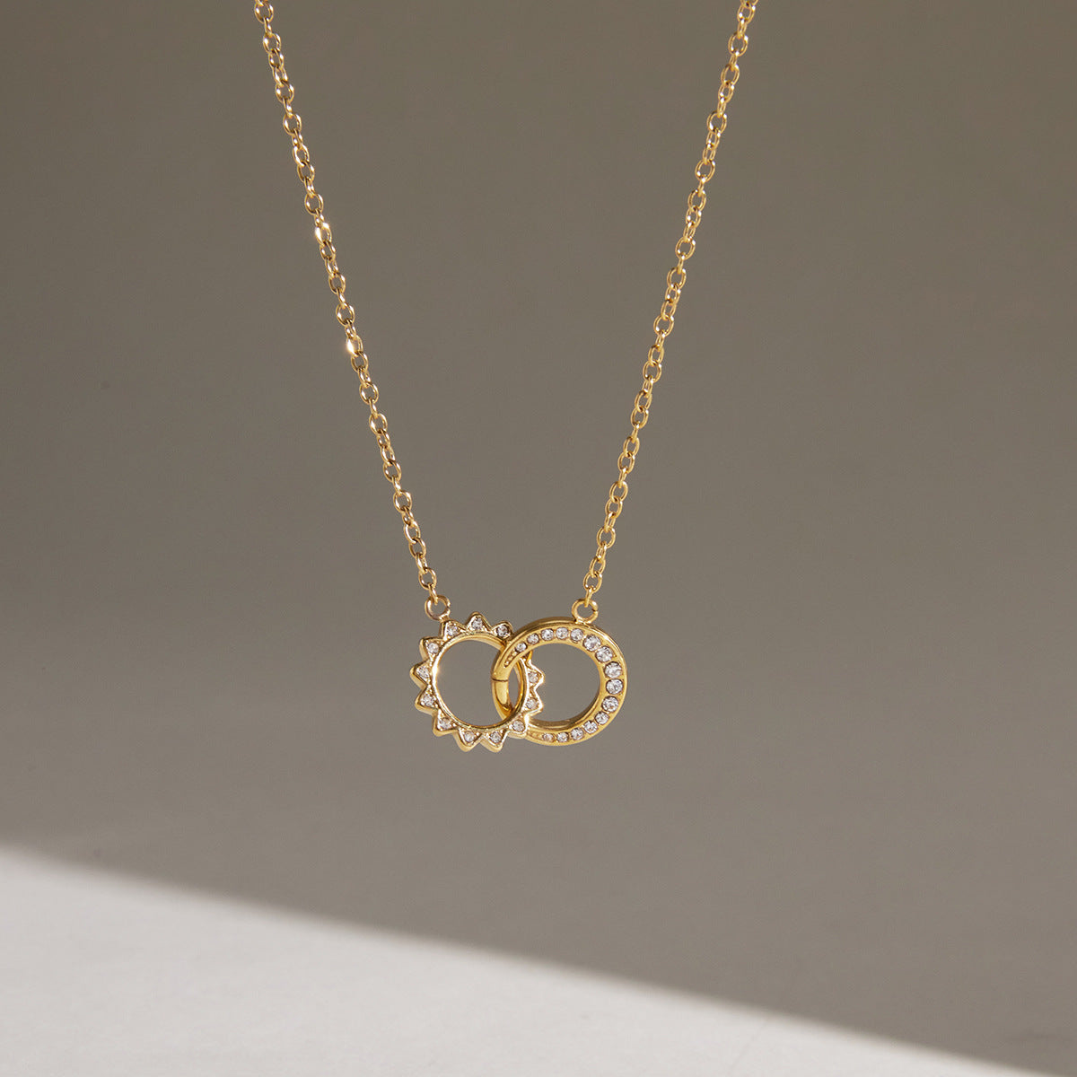 Gold tone interlocking circle necklace hanging against a pale background