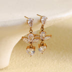 gold plated clear stone flower and heart drop earrings styled on cream