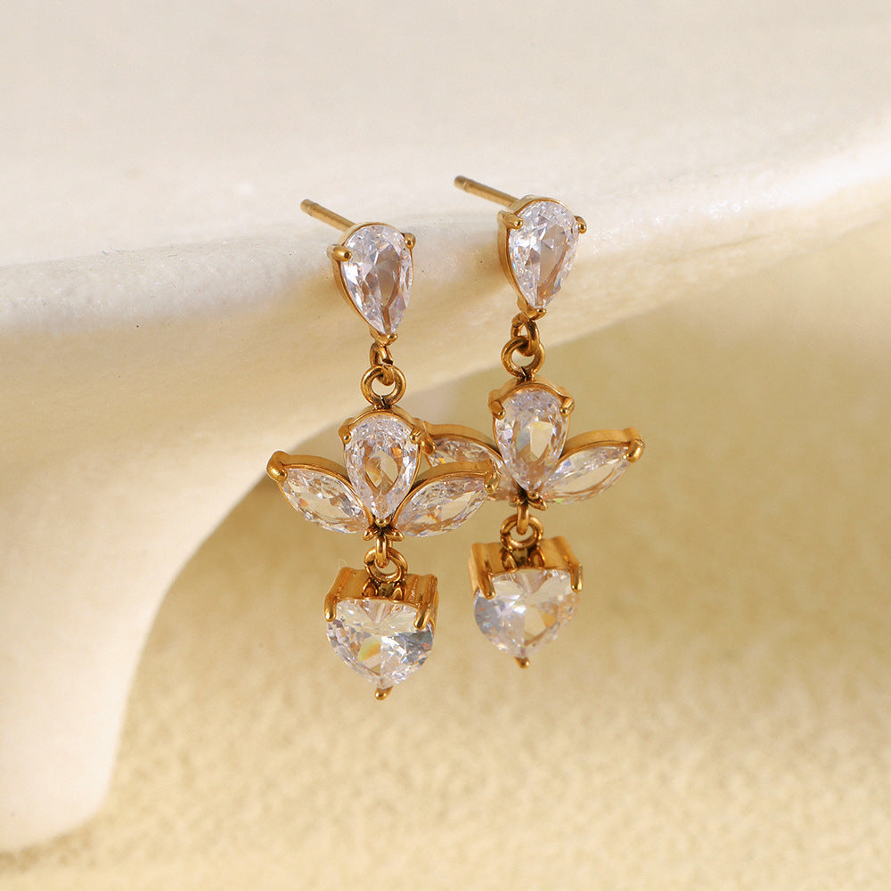 gold plated clear stone flower and heart drop earrings styled on cream
