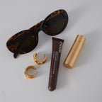 Textured gold finish hoops beside sunglasses and cosmetics
