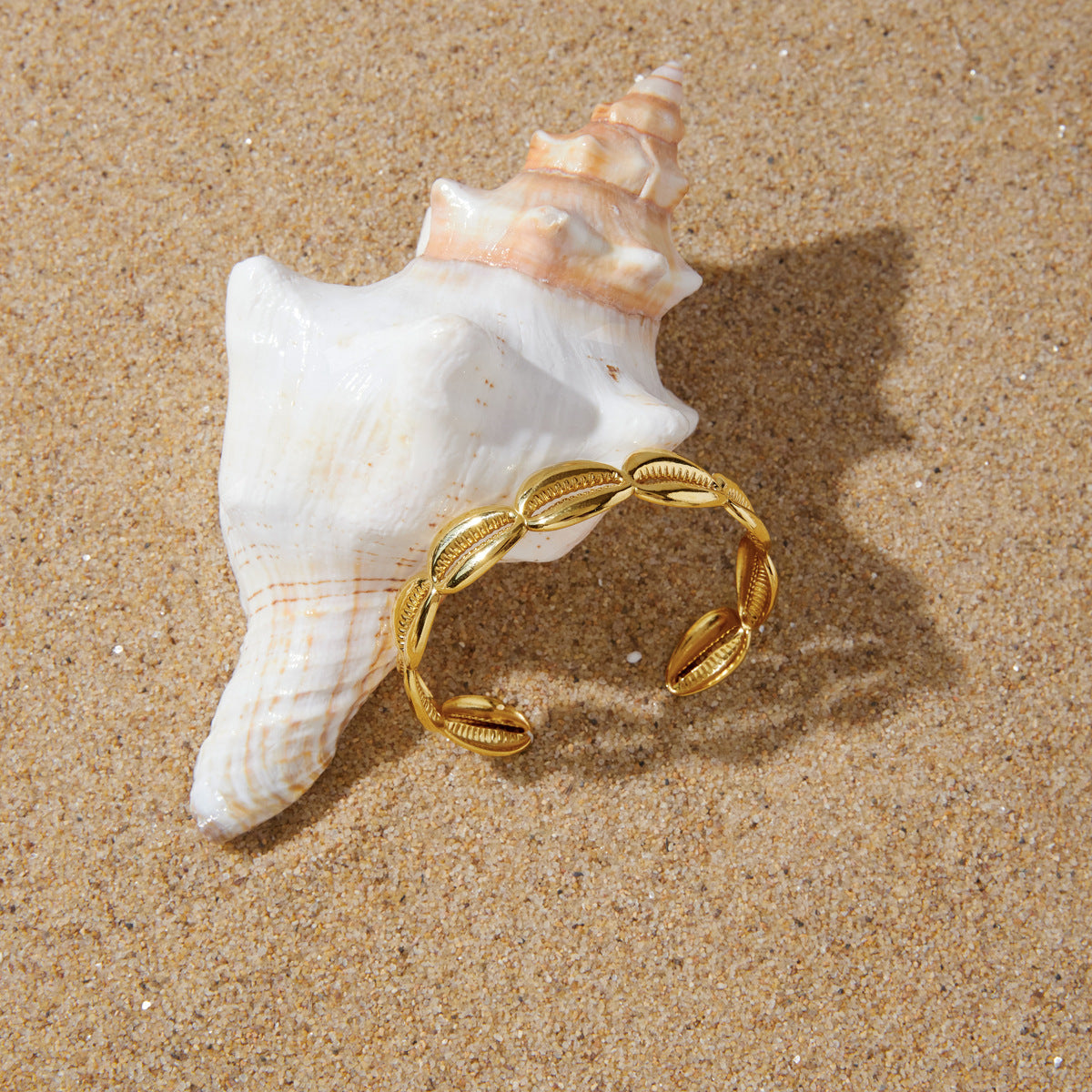 Gold tone shell motif cuff displayed on a spiral shell