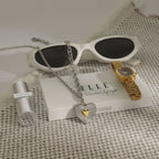 Silver-finish heart necklace displayed beside sunglasses