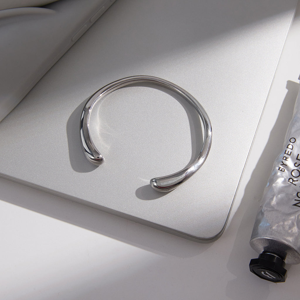 Silver-tone cuff with tapered rounded ends on a surface