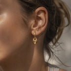 Gold tone pebble drop hoop worn at the earlobe