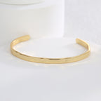 open brass bangle resting on a white jewelry display