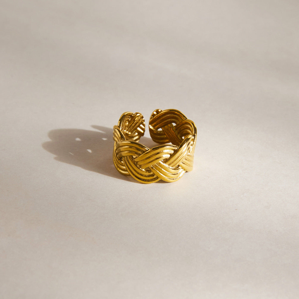 Wide braided gold tone ring standing on a pale surface