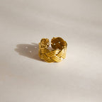 Wide braided gold tone ring standing on a pale surface