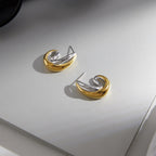 Mixed-tone curved earrings resting on a gray surface