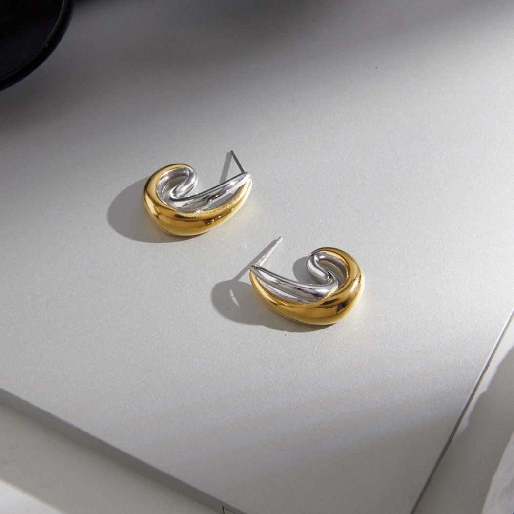 Mixed-tone curved earrings resting on a gray surface