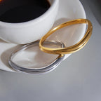 Curved clasp bangles beside a cup