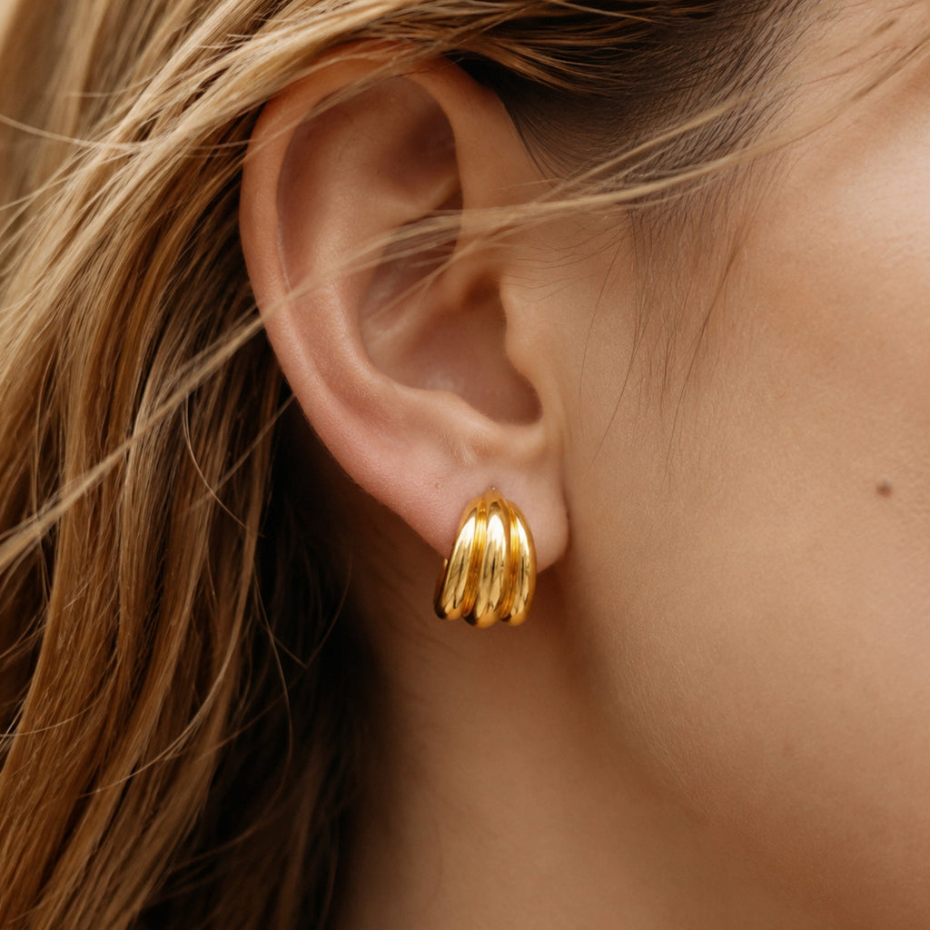 Gold tone triple ridge hoop worn on an ear