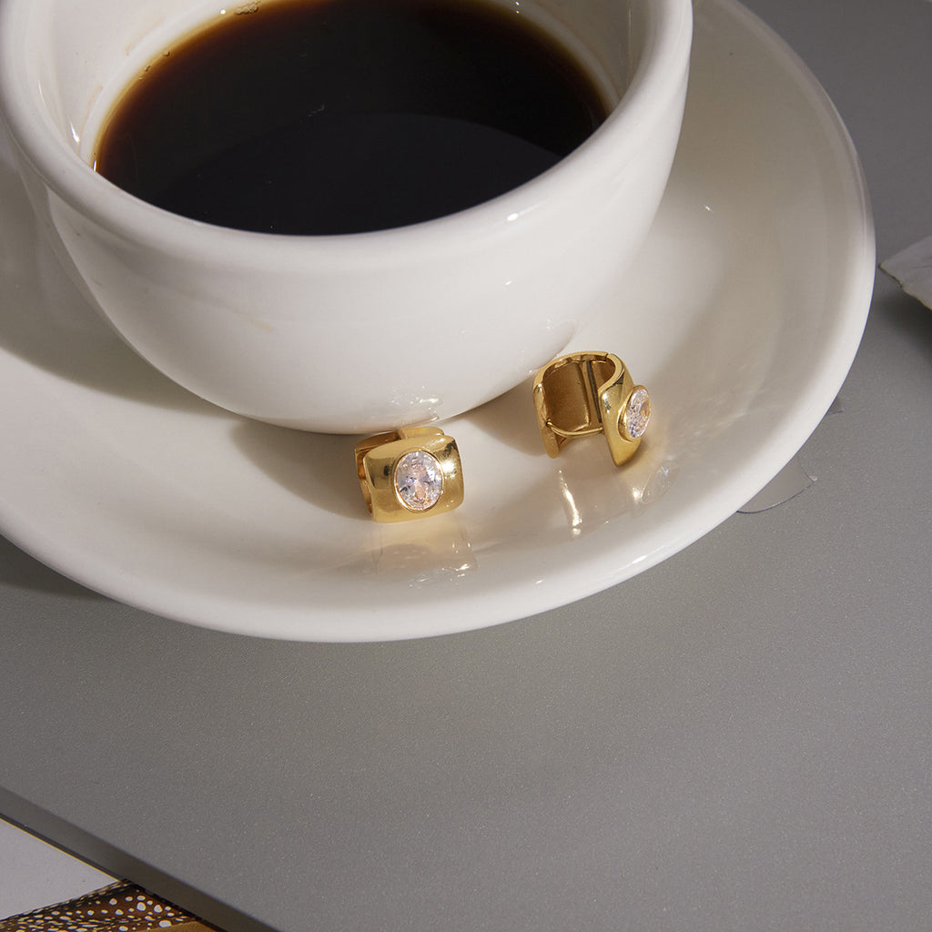 pair of oval clear-stone huggie earrings beside a coffee cup