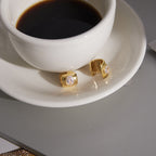 pair of oval clear-stone huggie earrings beside a coffee cup