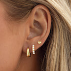 Model wearing gold-tone stainless steel huggie earrings with blue beads