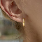 Close-up of a slim gold finish twisted hoop worn