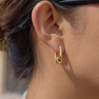 Gold-finish oval hoop with three stone ring charms shown on the ear