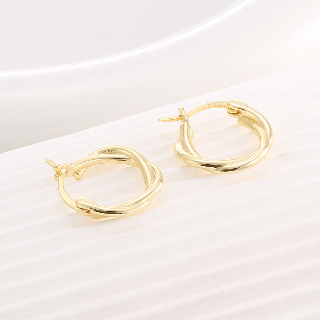 gold plated offset hoop earrings resting open on a ribbed surface