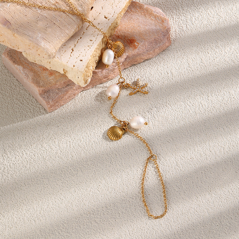 Gold tone foot chain with shell and starfish charms on a pale surface