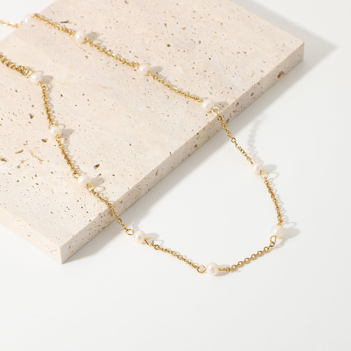 Spaced pearl necklace arranged beside a stone slab