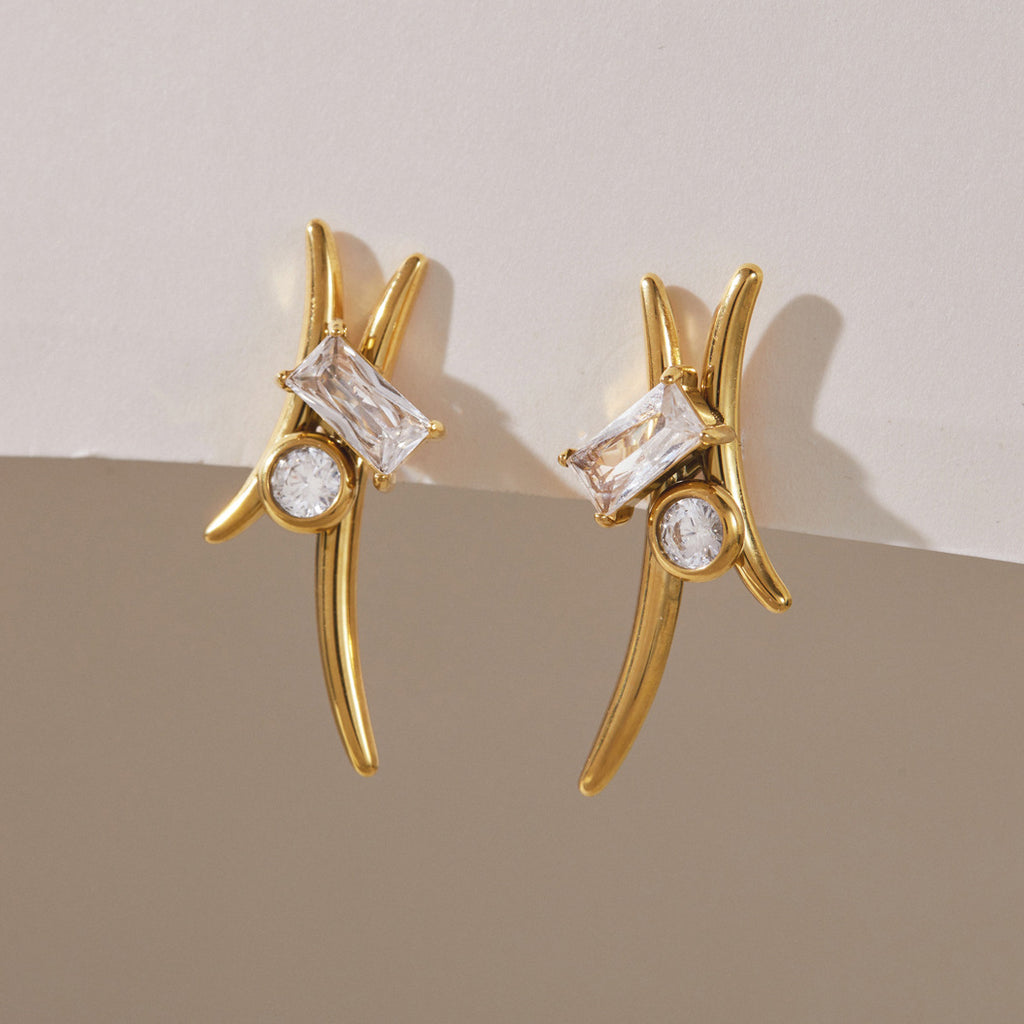 Pair of sweeping gold-tone curve earrings on a textured surface