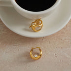 Side and rear of the hinged sculpted earrings beside a cup
