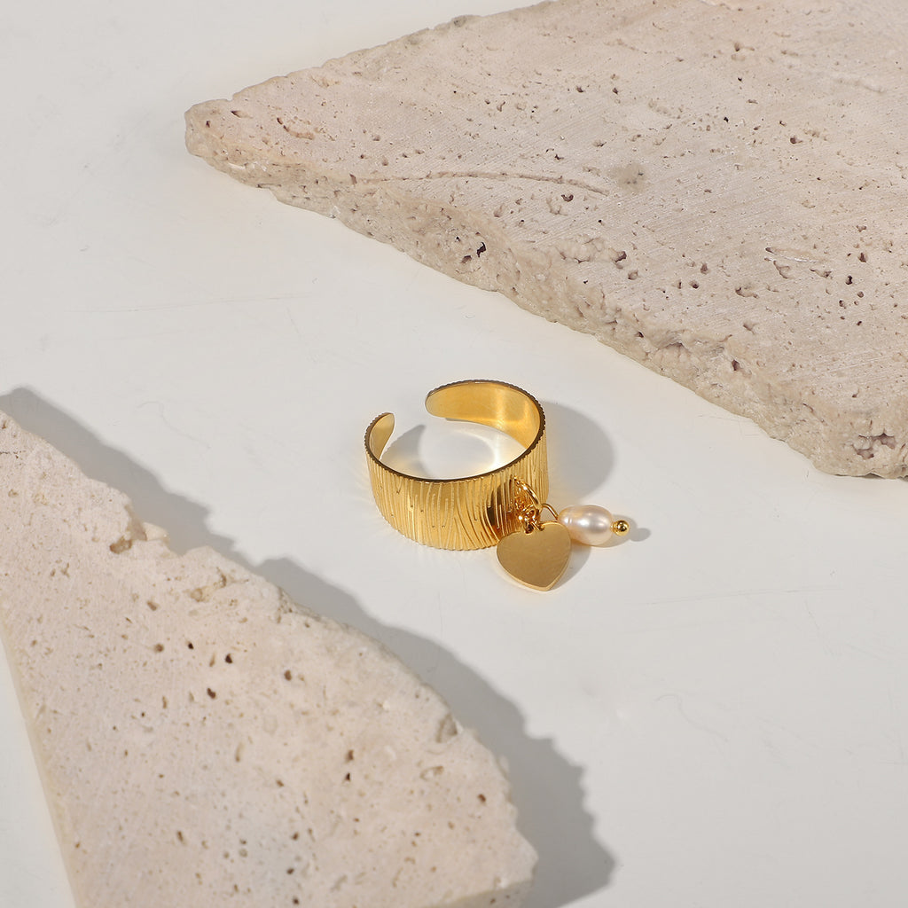 Stainless steel heart charm ring photographed between pale stone props