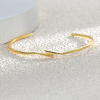 gold plated lightning bolt bangle resting on a textured surface