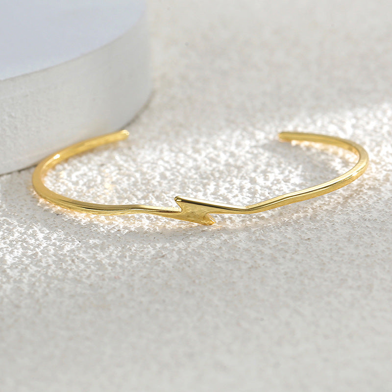 gold plated lightning bolt bangle resting on a textured surface