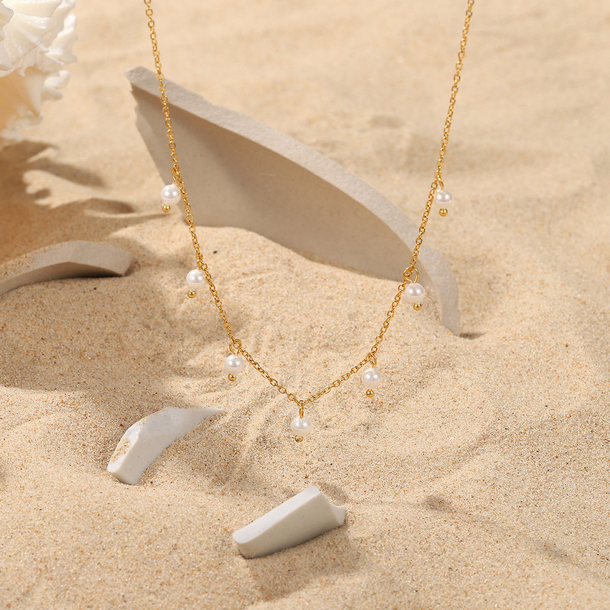 fine pearl-style station necklace arranged on a sandy display