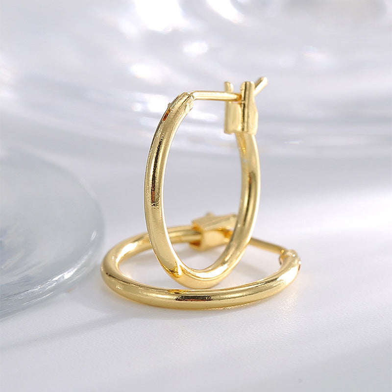 gold plated slim brass hoop earrings beside clear glass