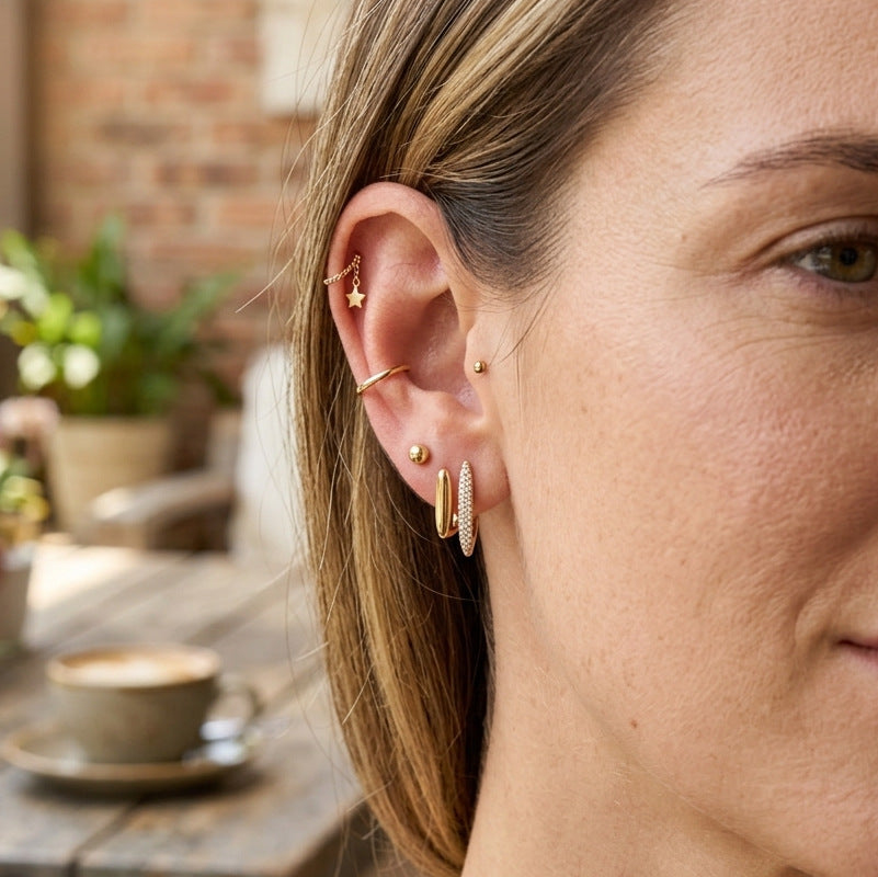 Slim gold tone earring styled with additional ear jewelry