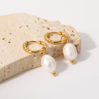 Twisted stainless steel pearl earrings on a stone display
