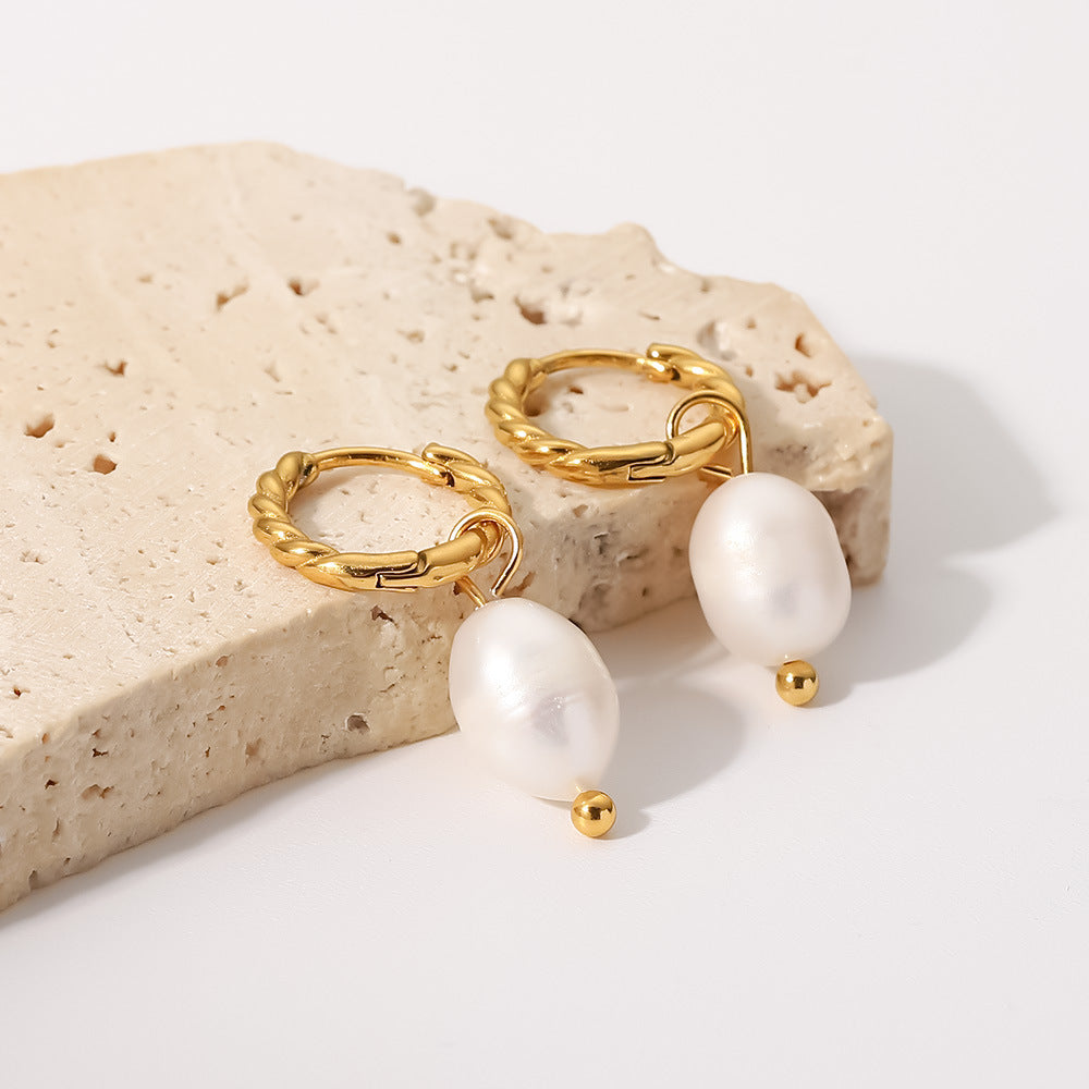 Twisted stainless steel pearl earrings on a stone display