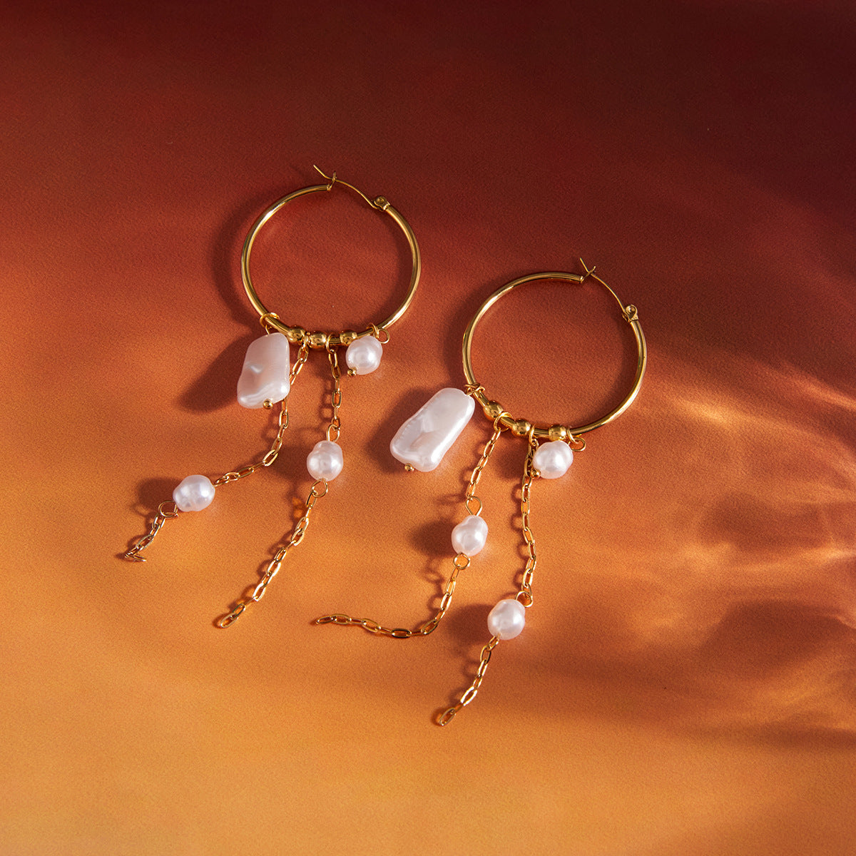 Pair of stainless steel faux pearl tassel hoops on rust-colored fabric