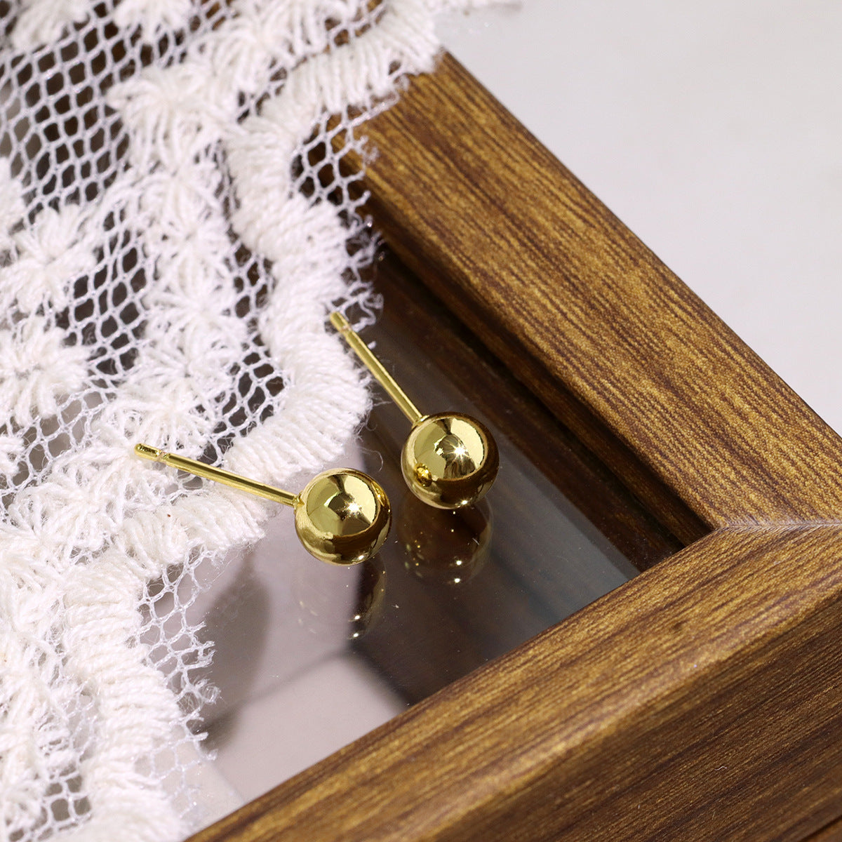 polished gold plated ball studs beside a wooden frame