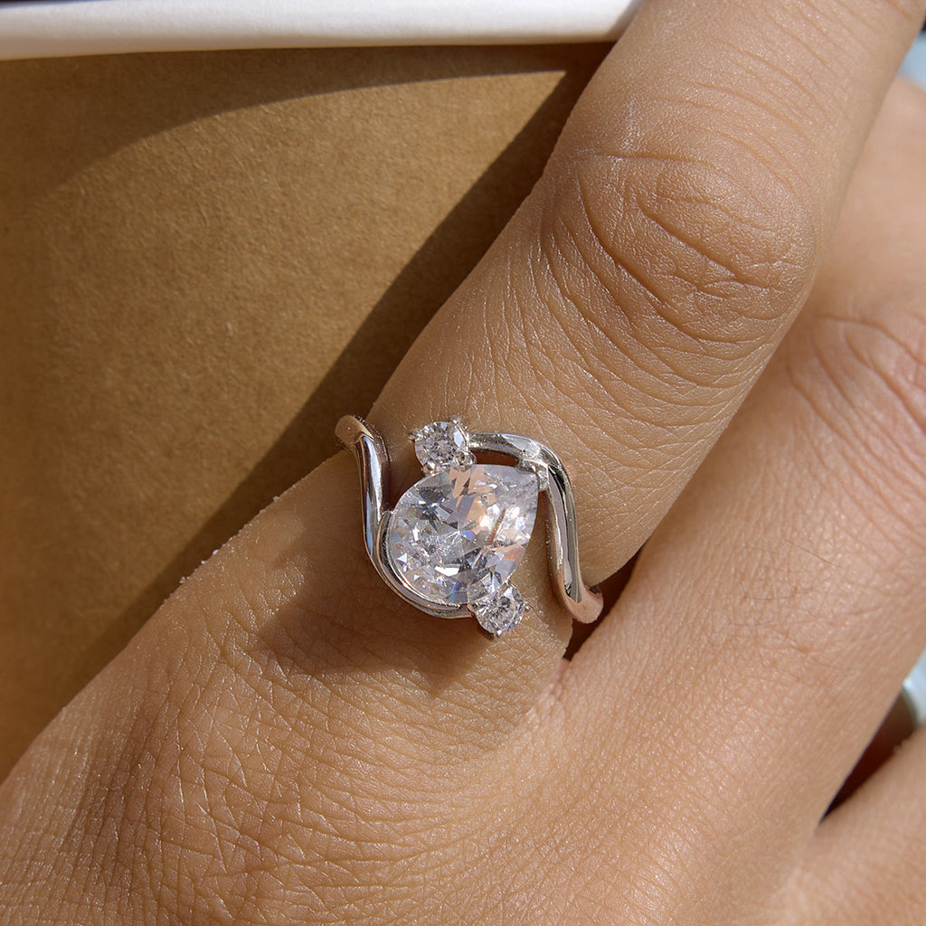 Silver-tone curved ring with clear pear center worn on a hand