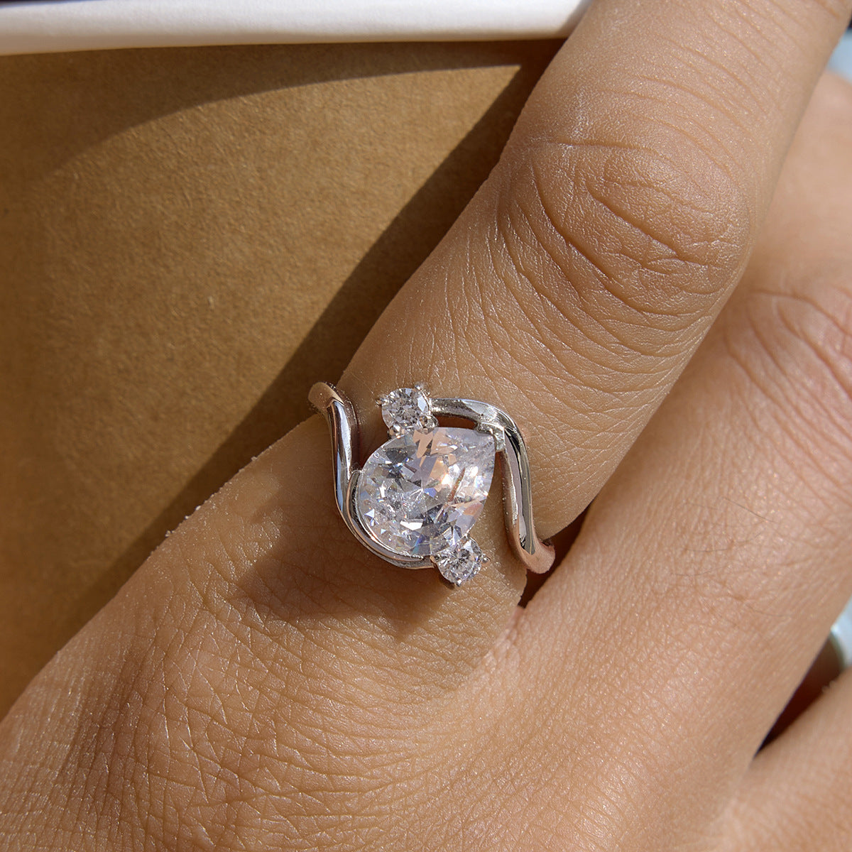 Silver-tone curved ring with clear pear center worn on a hand