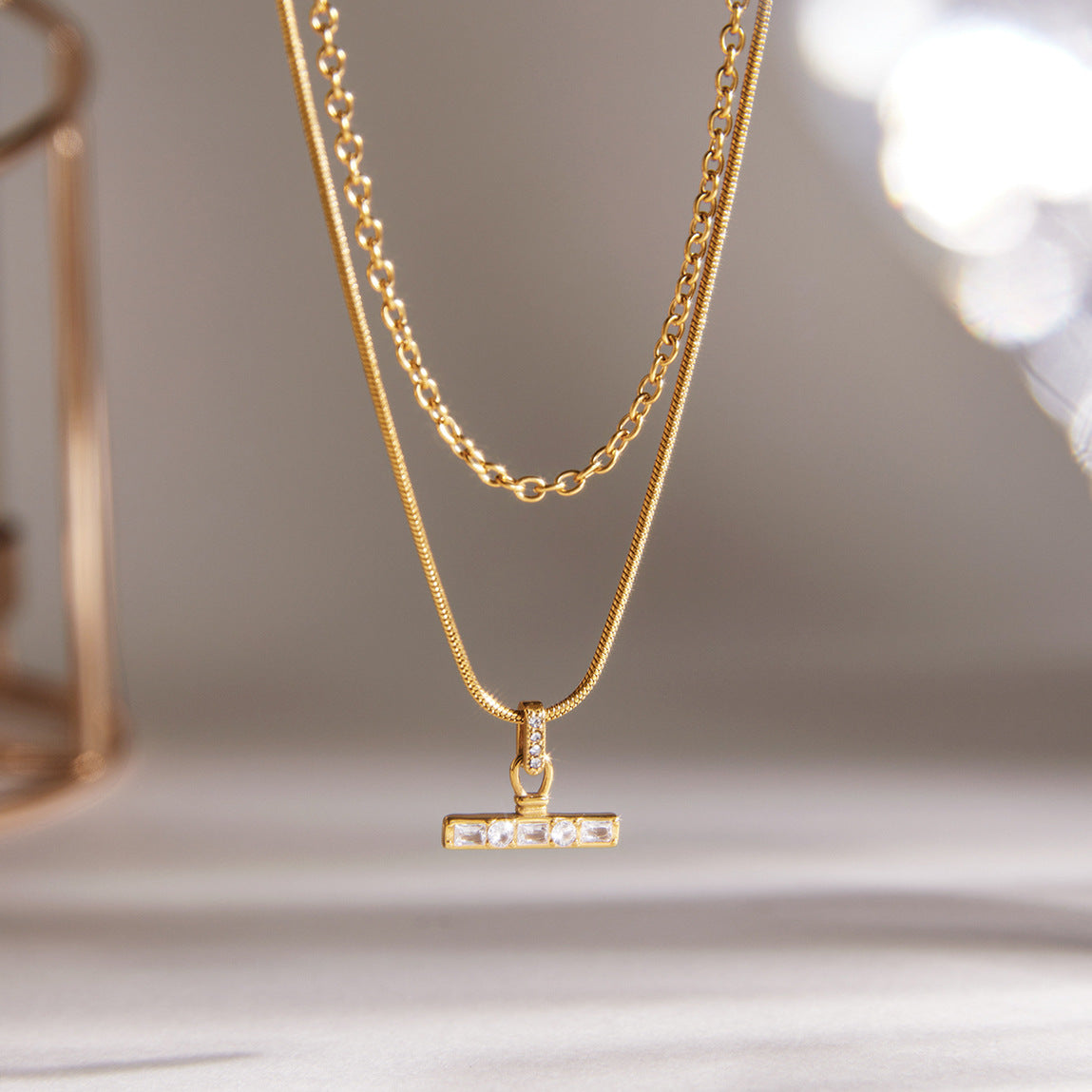Two-layer T-bar necklace hanging against a pale background