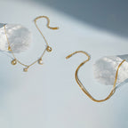 Two gold tone anklet designs displayed beside clear stones