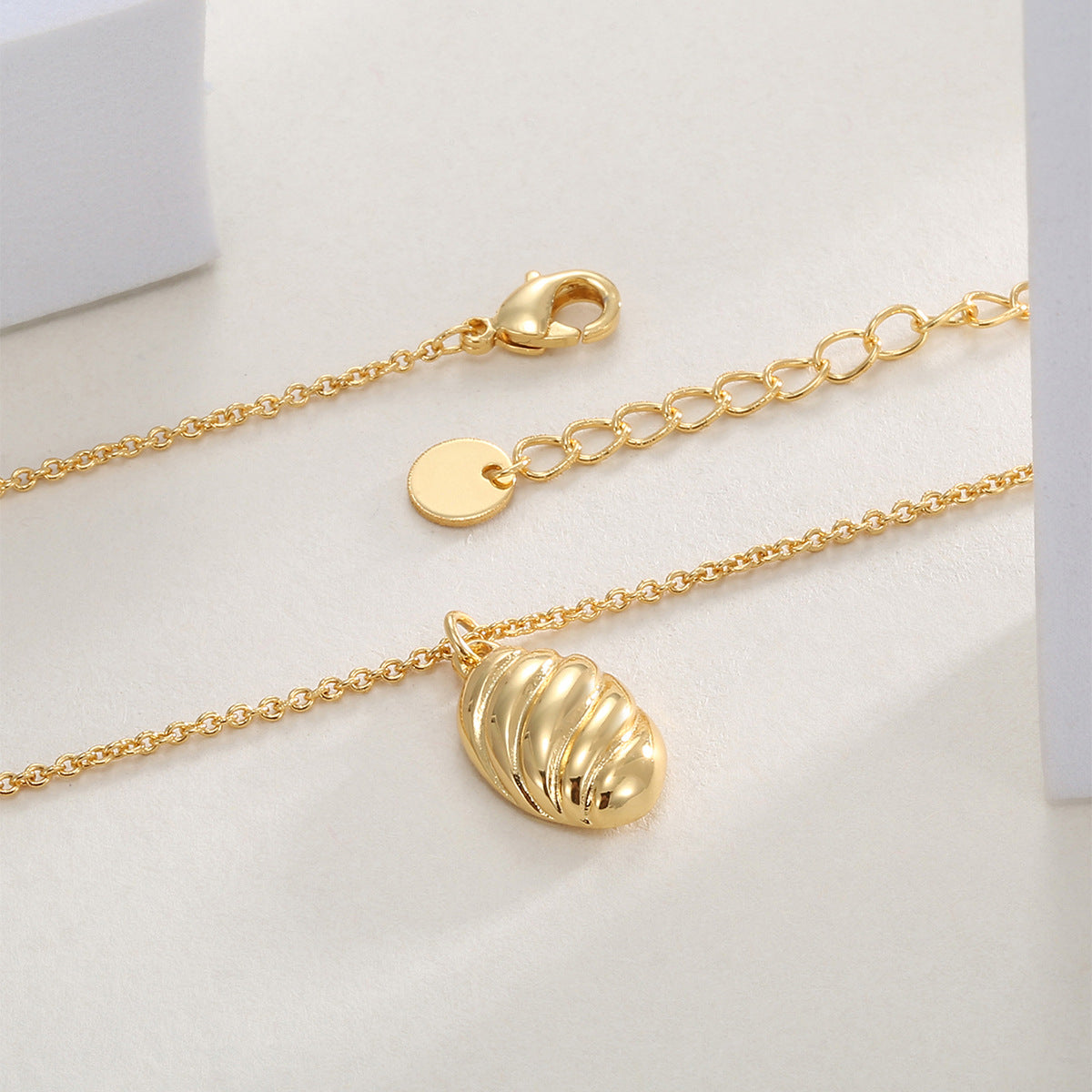 ribbed oval pendant necklace laid beside its lobster clasp and extender