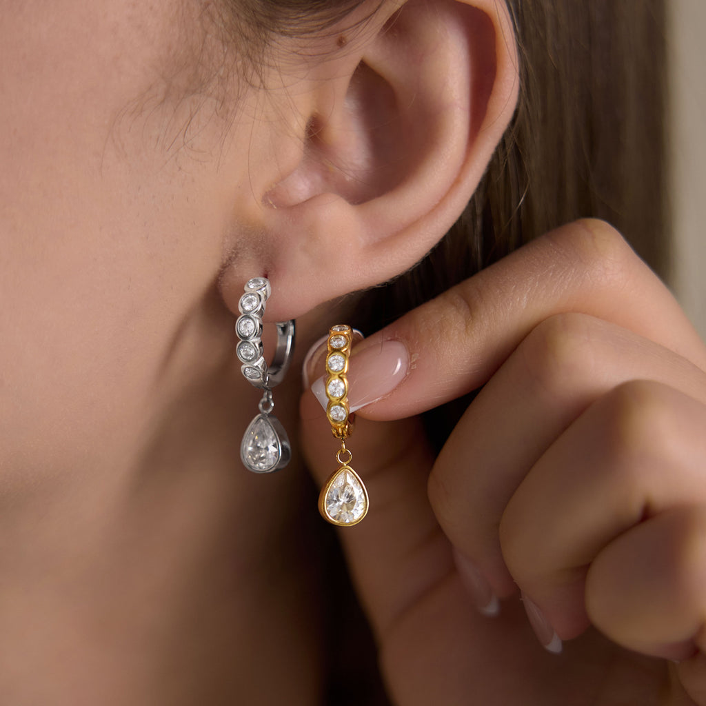 Silver tone teardrop huggie worn beside a gold tone version held in hand