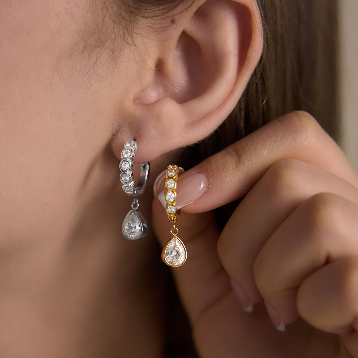Silver tone teardrop huggie worn beside a gold tone version held in hand