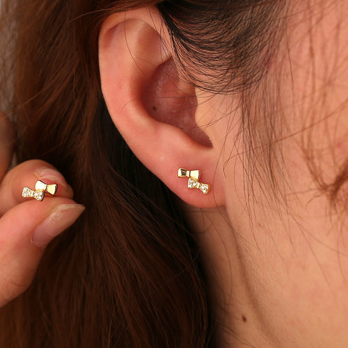 asymmetric bow stud earring with smooth and clear-stone loops worn on the ear