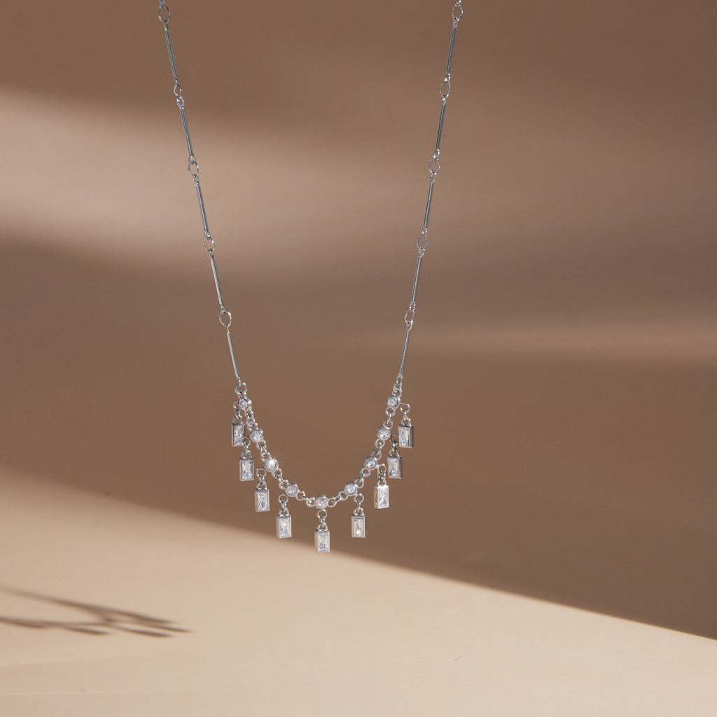 Silver tone fringe necklace hanging against a pale background