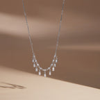 Silver tone fringe necklace hanging against a pale background