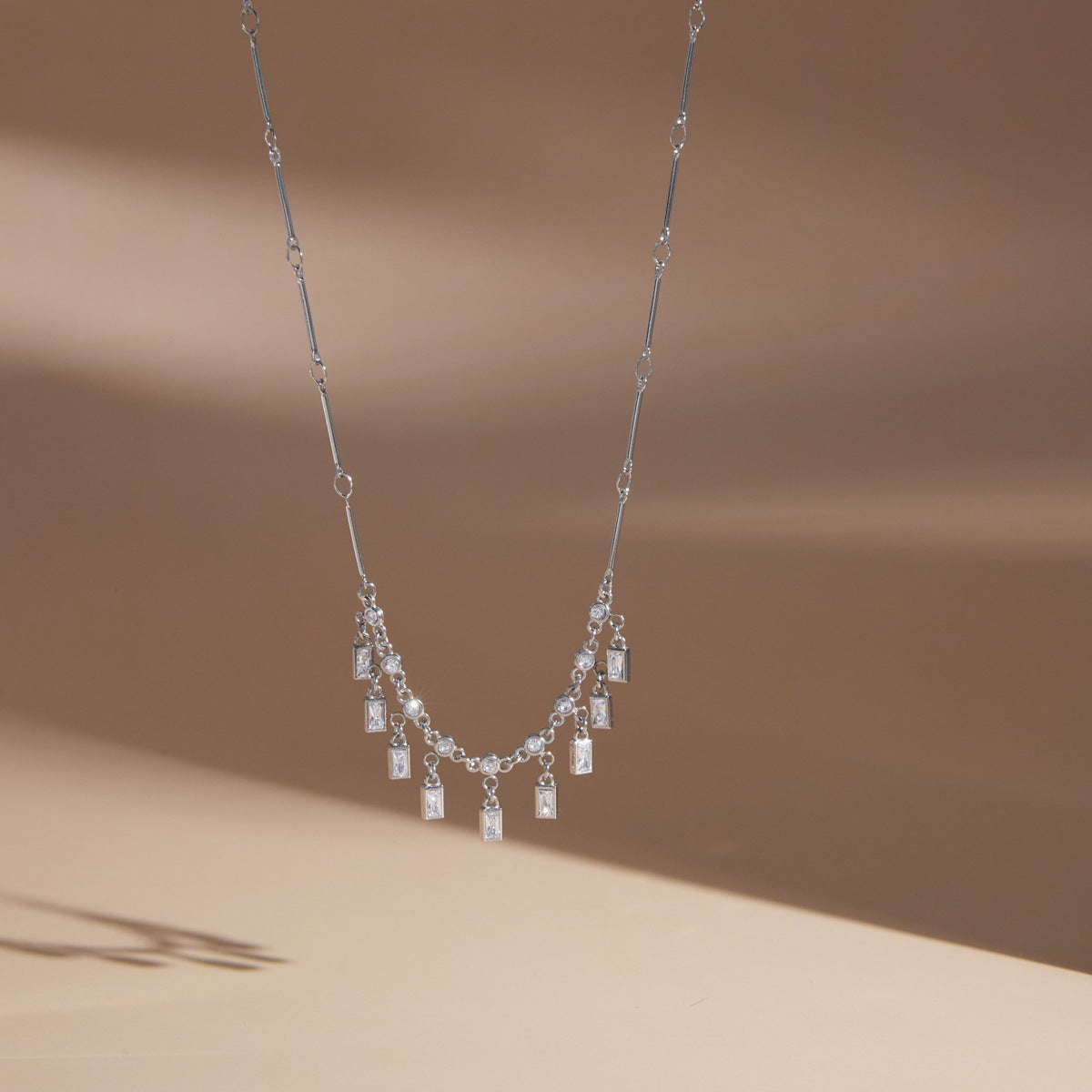 Silver tone fringe necklace hanging against a pale background
