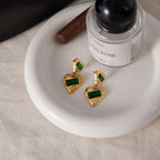 Pair of gold plated green stone heart earrings on a tray