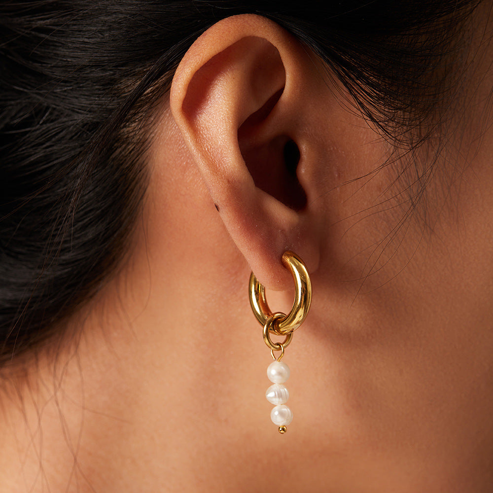 Gold-tone hoop with three-pearl drop worn on an ear